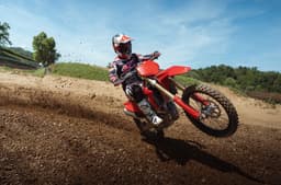 Rider powers the Desmo250 MX through a berm, kicking up dirt on a motocross track.
