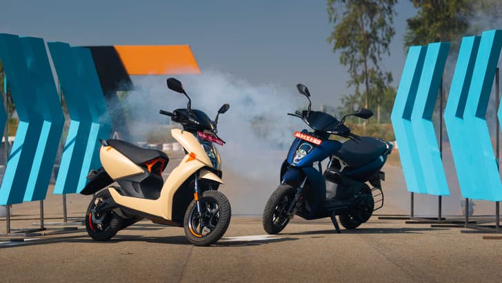 Two Ather 450X scooters parked with blue smoke in the air in the background
