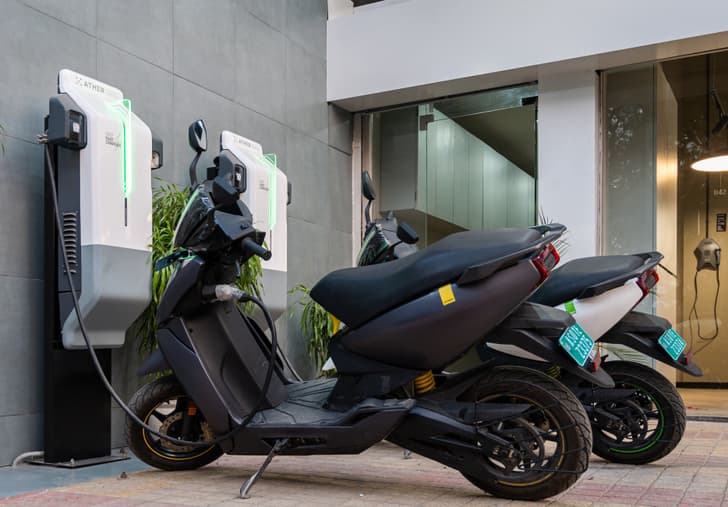 Two Ather 450X scooters parked and charging from two fast chargers