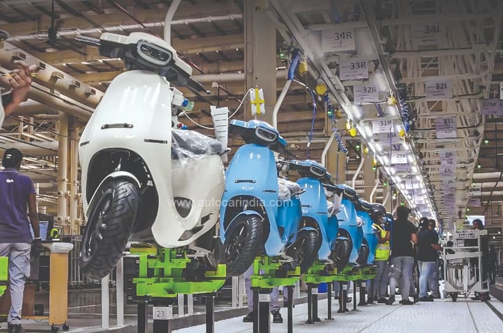 Image of Ola scooters coming off the production line with employees in the background