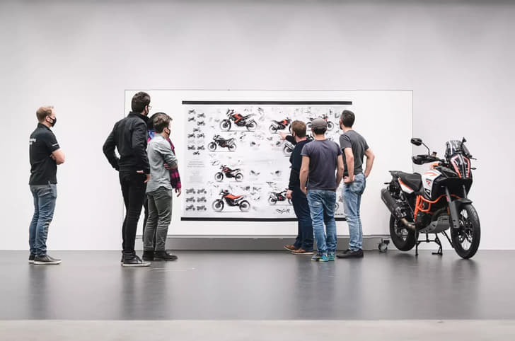 Designers looking at a drawing board with several KTM design sketches and a KTM 890 Adventure parked next to it