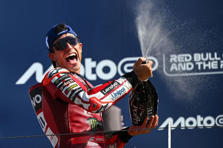 A podium shot showing Marc Marquez celebrating his win with prosecco.